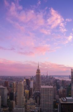 the city skyline is lit up at dusk with pink clouds in the sky and skyscrapers