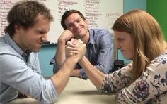 two men and a woman sitting at a table holding hands