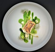 a white plate topped with green vegetables and fish on top of sauced broccoli