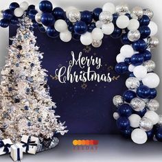 a christmas tree and balloon arch in front of a blue backdrop with white and silver balloons