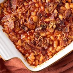 a casserole dish filled with beans and bacon on top of a red cloth