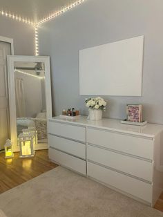 a white dresser sitting in a bedroom next to a mirror and lights on the wall