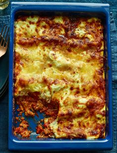 a casserole dish with meat and cheese in it on a blue plate next to utensils