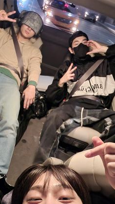 two people sitting in a car with one pointing at the camera and the other holding his hand up