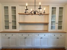 an empty room with white cabinets and wood flooring in the center is a chandelier