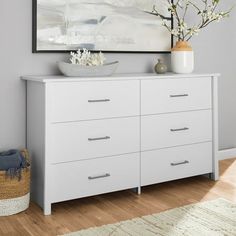 a white dresser sitting in a room next to a painting on the wall and a vase with flowers