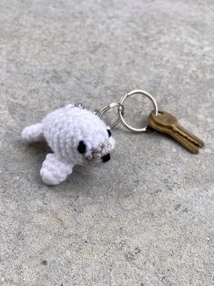 a white stuffed animal keychain sitting on top of a cement floor next to a pair of keys