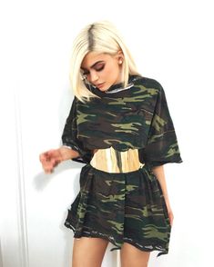 a woman with blonde hair wearing a camo print dress and gold belted boots