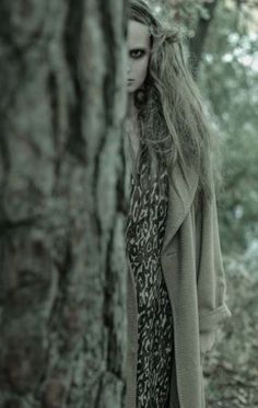 a woman with long hair standing next to a tree in the woods wearing a leopard print dress