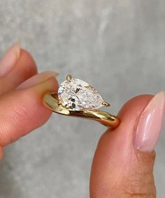 a woman's hand holding a yellow gold ring with a pear shaped diamond on it