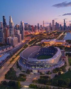 an aerial view of a large stadium in front of the chicago skyline at night with lights on