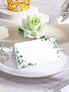 a white plate topped with a card and a flower next to a gold tiara