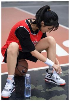 a young woman sitting on top of a basketball court next to a bottle of water