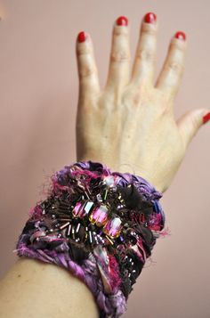 a woman's hand with red nail polish holding onto a bracelet that has beads and sequins on it