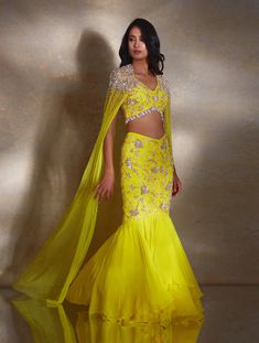 Yellow sleeveless embellished blouse paired with a fitted fishtail skirt & georgette layer featuring hand-embellished champagne & silver daffodils & paired with a net cape hand embellished with pearls & glass beads & tassels.From Shloka Khialani's Winter Sun collection.DELIVERY TIMEPlease allow 6-8 weeks for your outfit to arrive.FABRIC DETAILSGeorgette, NetProfessional cleaning only. Tassel Skirt Outfit, Latest Bridal Lehenga Designs, Beads Tassels, Haldi Outfits, Bridal Lehenga Designs, Latest Bridal Lehenga, Indian Outfits Lehenga, Tassel Skirt, Net Dress