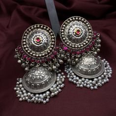 Introducing the Garba Jhumka Earrings by Quirky Fashions--an exquisite blend of tradition and style, perfect for the upcoming Navratri celebrations. These antique silver jhumkas are crafted with a big round stud adorned with a shimmering stone, accompanied by the delightful chime of ghungroo at the bottom. The grand hanging jhumka, with its intricate hand-hammered floral prints, features a moti hanging below, adding an elegant touch to your festive ensemble. Get ready to dazzle this Navratri wit Festive Heavy Temple Jewelry Earrings, Bollywood Style Kundan Chandbalis In Dual-tone, Bollywood Style Dual-tone Kundan Chandbalis, Traditional Dual-tone Danglers, Festive Dual-tone Kundan Chandbalis, Bollywood Style Anarkali Set For Festive Occasion, Traditional Dual-tone Earrings For Diwali, Navratri Chandbalis With Intricate Design, Bollywood Style Silver Anarkali Set For Eid