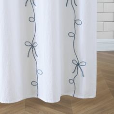 a white shower curtain with blue embroidery on the top and bottom, hanging from a wooden floor