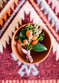 a small bowl filled with oranges and flowers on top of a red area rug