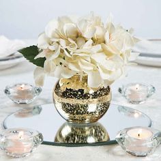 a vase filled with white flowers sitting on top of a table next to candles and plates