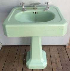 a green pedestal sink sitting on top of a wooden floor