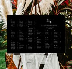 a black and white wedding seating plan on a easel in front of some plants