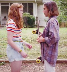 two young women standing in front of a house talking to each other with skateboards