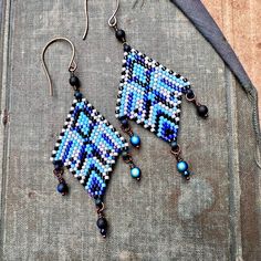 a pair of blue and black beaded earrings sitting on top of a piece of cloth