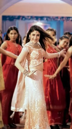 a woman in a white and gold dress dancing with other women wearing red dresses behind her