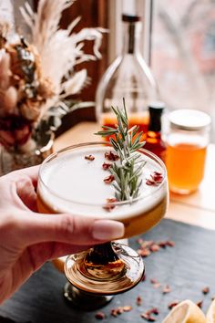 a person holding a wine glass with a rosemary sprig on it