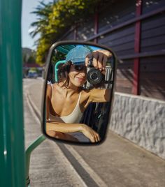 a woman taking a selfie in the side mirror of a car with her camera