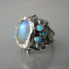 A unique antique style hand crafted ring for brides to be!A rainbow moonstone ring that will make you feel like a real queen on your special day! This moonstone ring features a sterling silver band and handcrafted setting of fascinating rainbow moonstone gemstone, and small moonstones and lab opals stones on both sides.Measurements:Center stone - 10mm / 14mmSize:Moonstone queen ring is adjustable to any size, it has a small opening so you can adjust it to fit your finger.Materials: Stone: moonst Witchy Engagement Rings, Big Statement Rings, Queen Rings, Rings Gemstone, Engagement Rings Affordable, Moonstone Engagement, Wedding Rings Halo, Rainbow Moonstone Ring, Alternative Engagement Rings