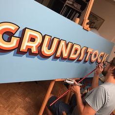 a man working on a sign that says grundstool in orange and blue