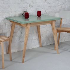 a table and two chairs in front of a white brick wall with red vases on it