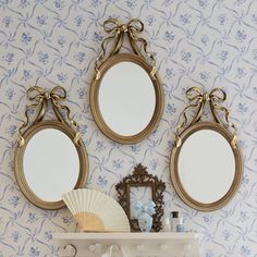 three mirrors are hanging on the wall above a shelf with a fan and other items