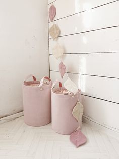 two pink storage baskets sitting next to each other on top of a white floor covered in leaves