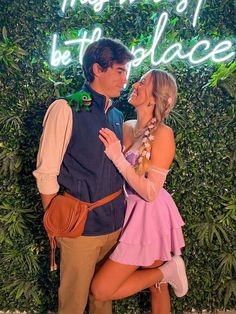 a man and woman standing next to each other in front of a wall with plants