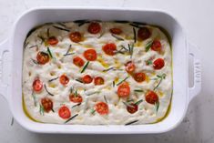 a white casserole dish with tomatoes and herbs on top, ready to be eaten