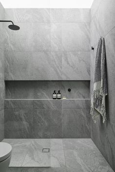 a white toilet sitting next to a walk in shower under a skylight on top of a tiled wall