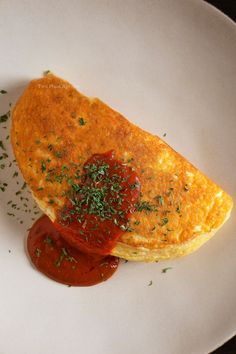 an omelet on a plate with ketchup and parsley sprinkled