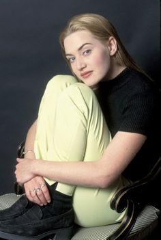 a woman sitting on top of a chair with her legs crossed and looking at the camera