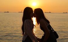 two young women standing next to each other near the ocean with boats in the background