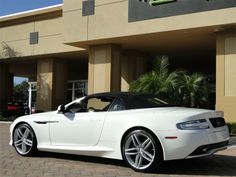 a white sports car is parked in front of a building with palm trees behind it