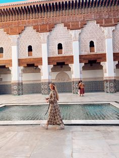 a woman in a long dress is walking by a pool