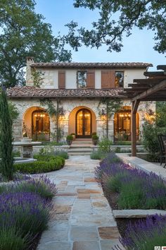 the front entrance to a house with lavender flowers in the foreground and stone walkway leading up to it