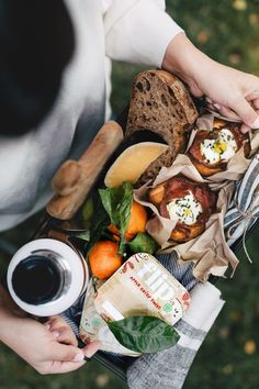 a person holding a basket full of food and drinks on top of a grass covered field