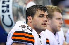 two football players sitting next to each other on the sidelines during a game, one is wearing an orange and white uniform