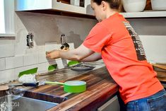 a woman in an orange shirt is making some food on the kitchen counter with green spatulas