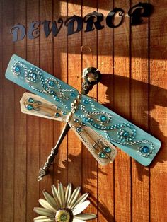 a blue dragonfly hanging from the side of a wooden wall next to a flower