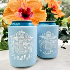 two blue can coolers sitting on top of a white table next to a flower