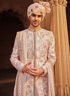 Step into elegance and make a statement on your special day with the Nude Pink Embroidered Sherwani Set, a masterpiece of traditional craftsmanship made from luxurious raw silk. The pink sherwani features an exquisite blend of colorful resham, zari, zardozi, and dabka work, with intricate detailing that showcases unique motifs exuding luxury and sophistication. The pastel hues lend an elegant, understated look. Paired with a matching kurta and pant, this ensemble offers both comfort and style. Completed with an embroidered stole, adding a refined touch that elevates the overall appeal. Perfect for the modern groom, this sherwani combines classic elements with contemporary flair, promising a truly regal appearance that will leave a lasting impression. Composition : Sherwani, Stole, Kurta an Pink Traditional Wear With Intricate Embroidery For Ceremonies, Pink Traditional Naqshi Sherwani, Pink Sherwani With Chikankari Embroidery For Reception, Pink Embroidered Bandhgala With Traditional Drape, Embroidered Pink Bandhgala With Traditional Drape, Traditional Pink Long Sleeve Bandhgala, Traditional Long Sleeve Pink Bandhgala, Pink Raw Silk Sherwani With Traditional Drape, Pink Bandhgala With Zari Work And Long Sleeves